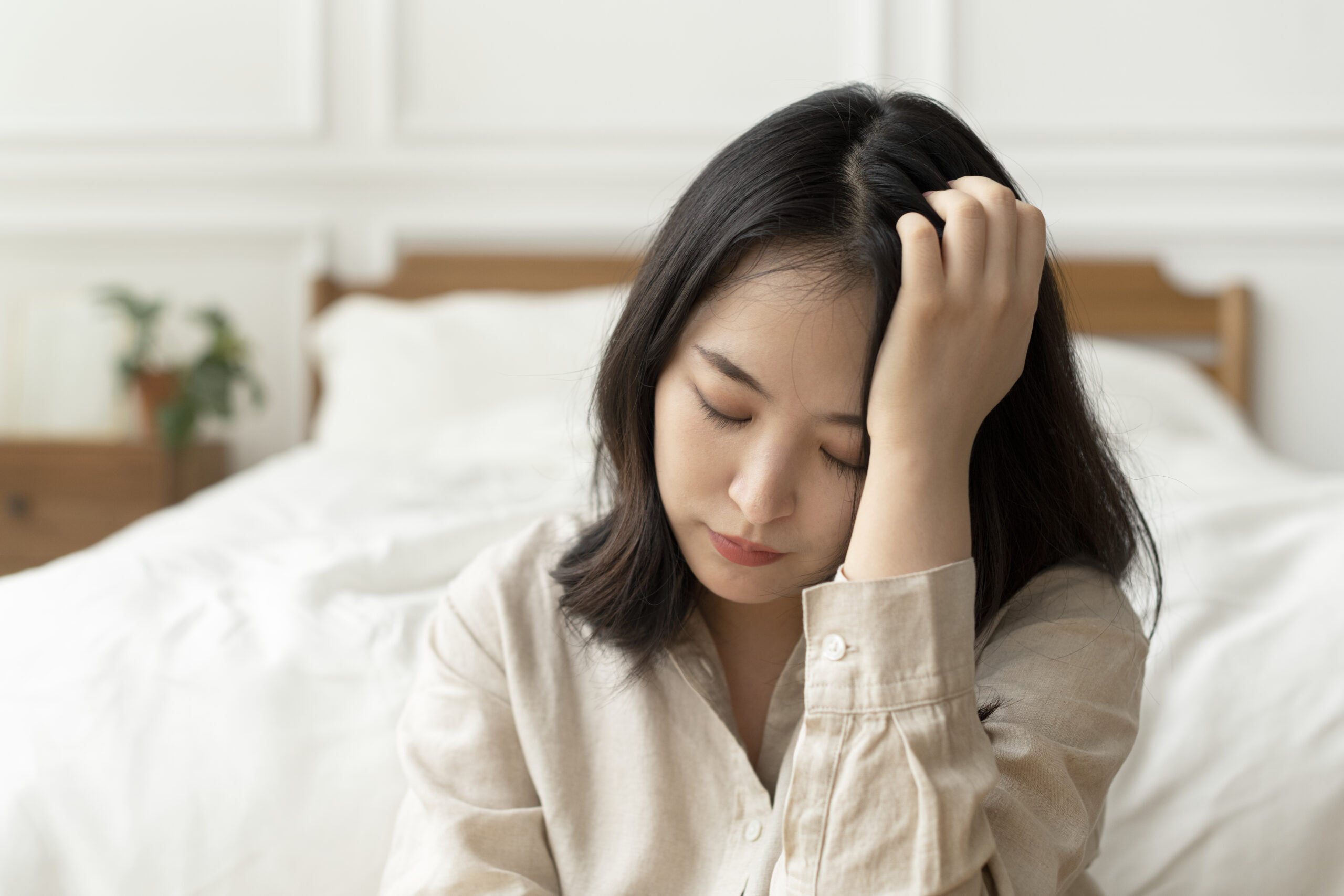 asian woman sitting sad by her bed scaled